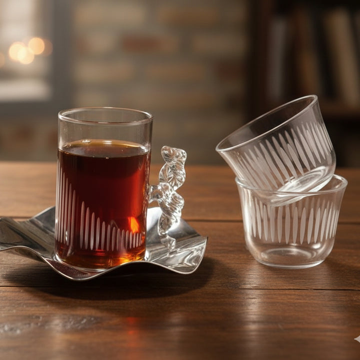 Clear glass cup with a handle containing a dark liquid on a wooden surface, with additional clear glass cups stacked nearby.