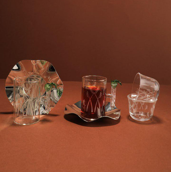 Set of glassware including a mirror, a glass with a red liquid, and another clear glass on a brown background.