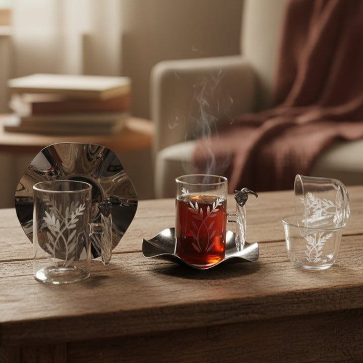 Tea set with a glass of steaming tea on a wooden table, surrounded by books and a blanket.