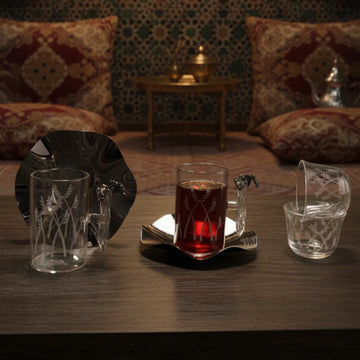 Glass of red liquid on a tray with decorative glasses on a wooden table, with a patterned wall and cushions in the background.