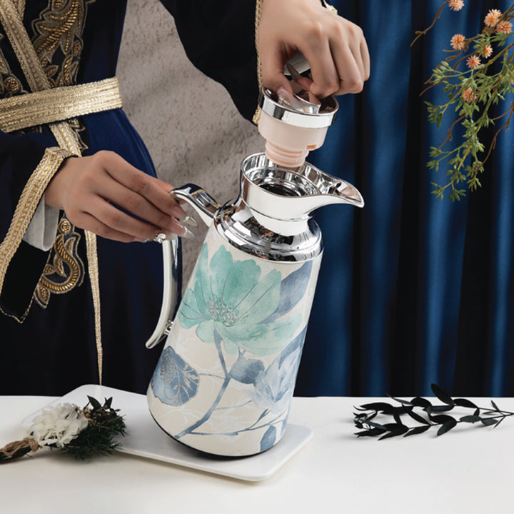 Person pouring from a decorative teapot with floral design on a white surface.