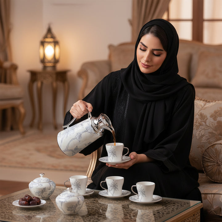 Woman in black hijab pouring tea into a cup in a cozy living room.