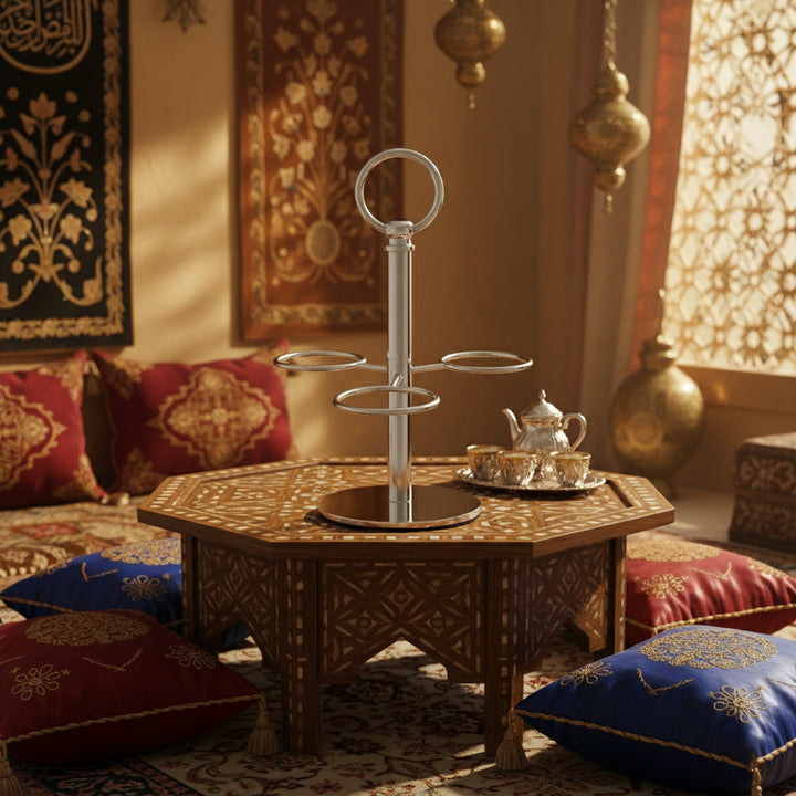Decorative tea set on a wooden stand in an ornate room with cushions and wall hangings.