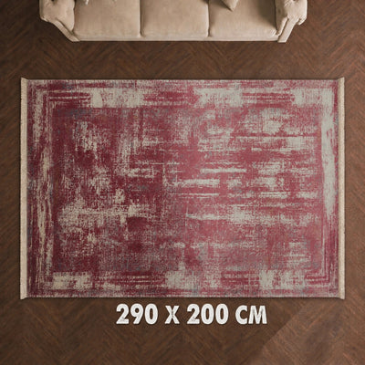 A rectangular area rug with a distressed, abstract pattern in dusty red and cream, shown from a top-down view on a dark wood herringbone floor. A beige sofa is partially visible at the top, and the text '290 X 200 CM' is overlaid at the bottom.