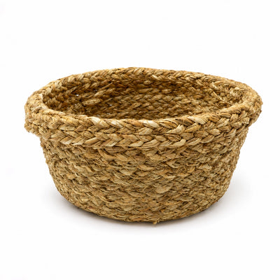 A round woven basket made from natural jute or seagrass fibers, featuring a sturdy braided texture and a small side handle, shown on a light gray background.