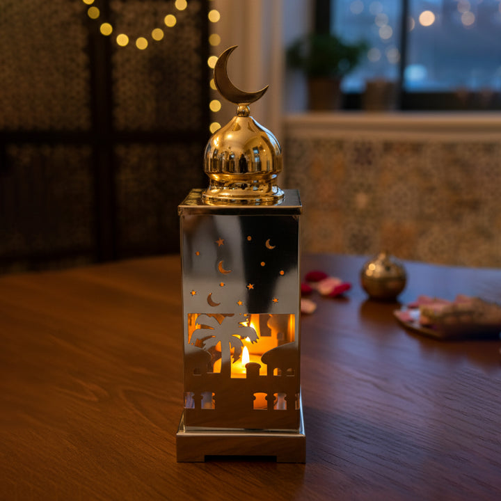 Decorative lantern with a crescent moon on top, lit from within, on a wooden surface.