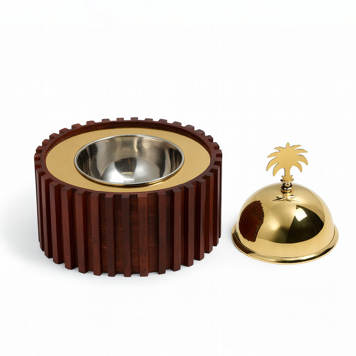 Decorative bowl with ribbed brown exterior and gold interior, next to a gold bell with palm tree design on a white background.