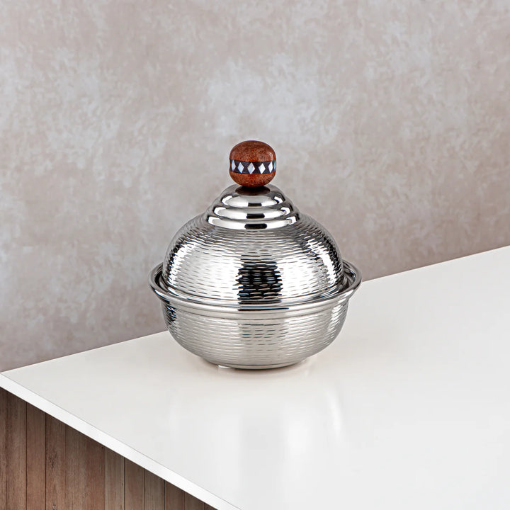 Silver textured bowl with a wooden knob on a white surface and beige wall background