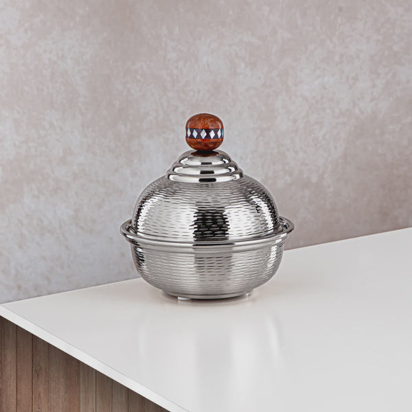 Silver decorative bowl with a textured lid on a white surface against a beige wall.