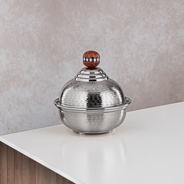 Silver decorative bowl with a textured lid on a white surface against a beige wall.