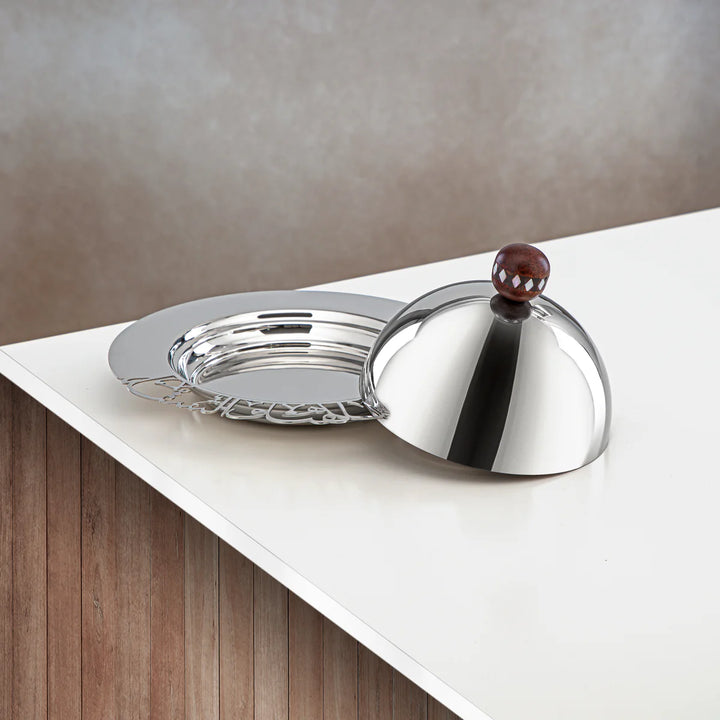 Silver bell-shaped object on a white surface with a wooden base.