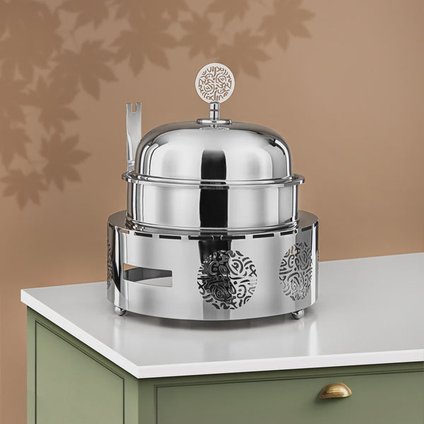 Stainless steel chafing dish on a countertop with a beige wall in the background