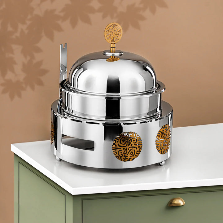 Stainless steel food warmer with decorative elements on a beige surface