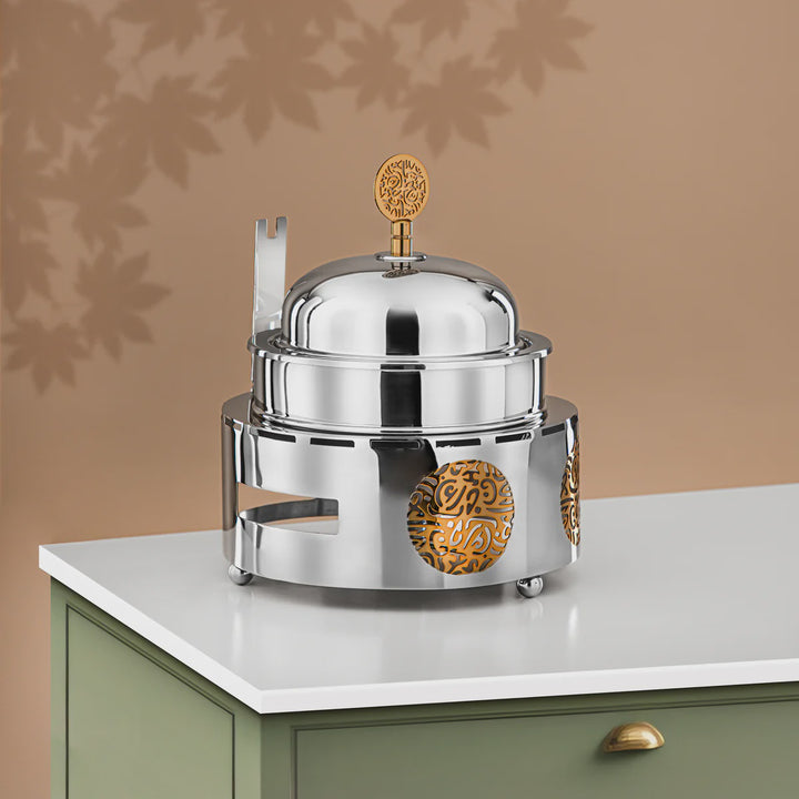 Stainless steel hot dish warmer with gold accents on a white surface against a brown background
