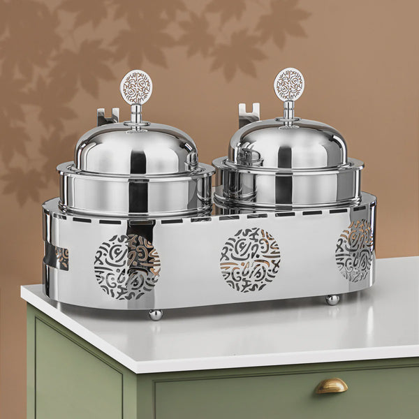 Silver serving dish with two covered compartments on a white surface against a brown background