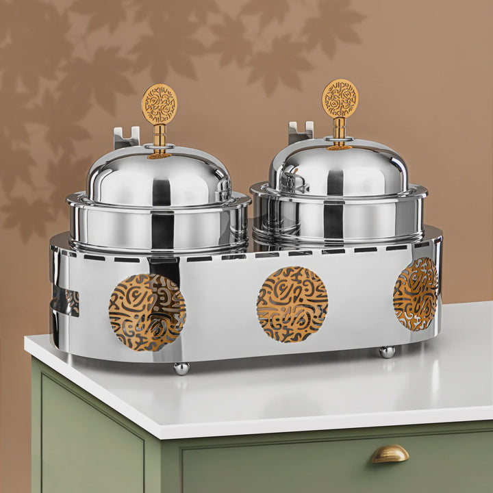 Stainless steel food warmers with decorative gold accents on a white surface.