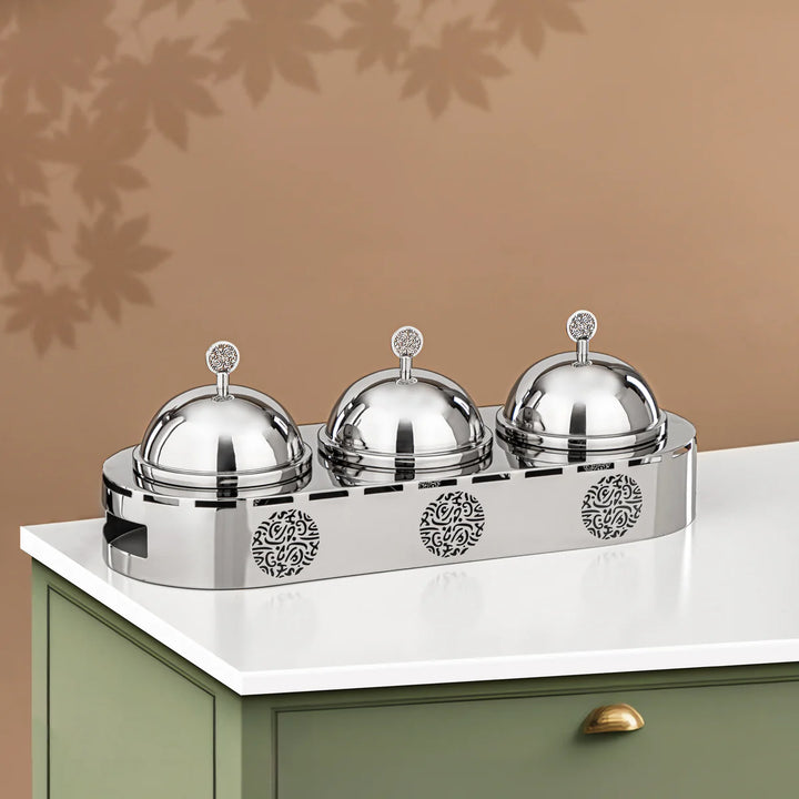 Set of three silver food covers on a decorative stand against a brown background