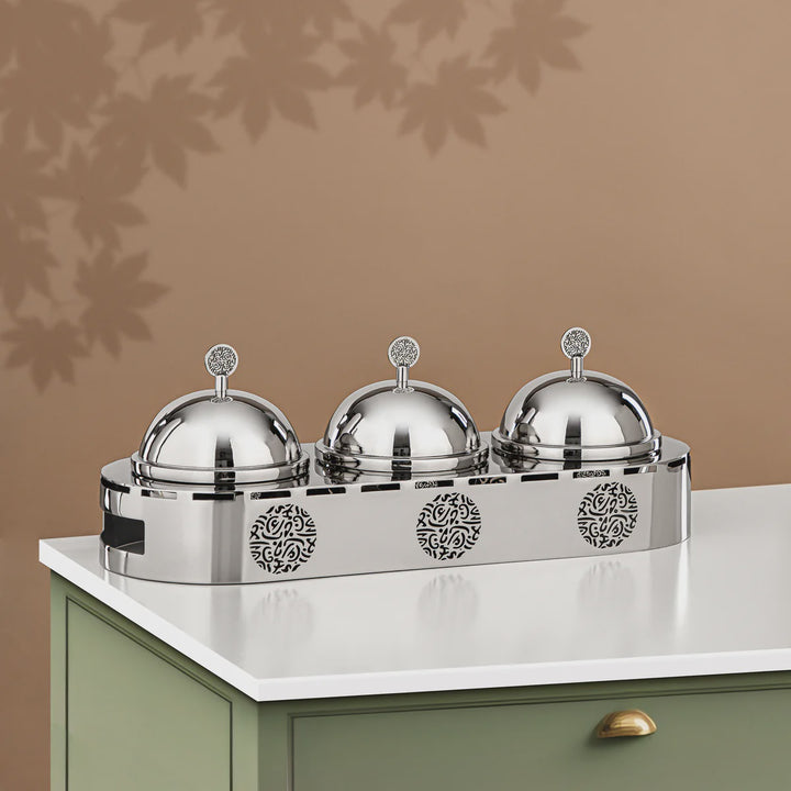 Silver three-dome food warmer on a white surface with a brown background