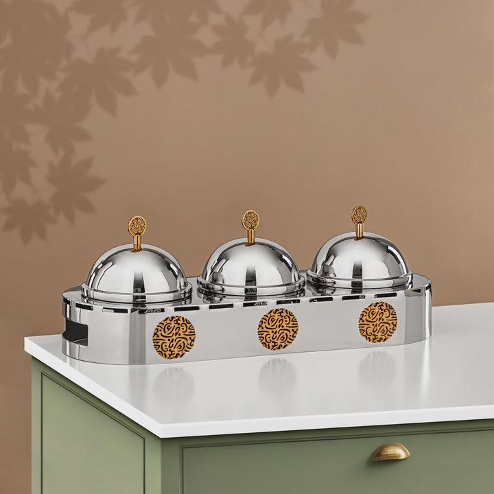 Three silver covered dishes with gold accents on a white surface against a brown background