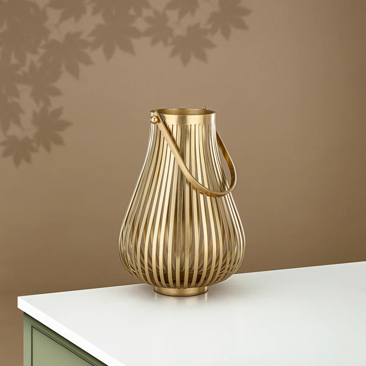 Gold decorative vase with ribbed design on a white surface against a brown wall.