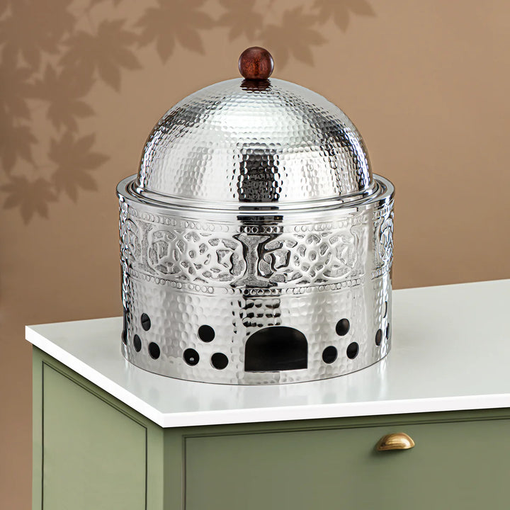Decorative metal container with a domed lid on a white surface against a beige wall.
