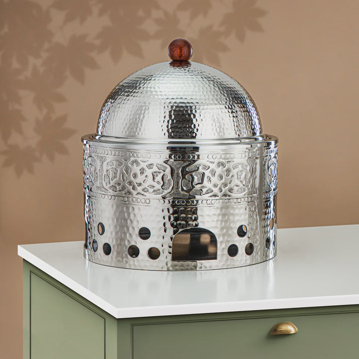 Decorative metal container with a domed lid on a white surface against a beige wall.
