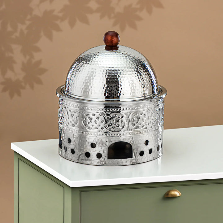 Decorative metal container with a domed lid on a white surface against a beige wall.