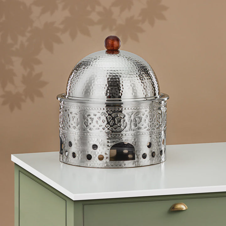 Decorative metal object with a textured surface on a white surface against a beige wall.