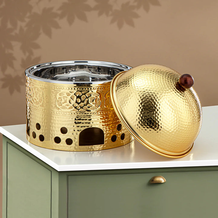 Gold decorative pot with intricate designs on a white surface against a beige background