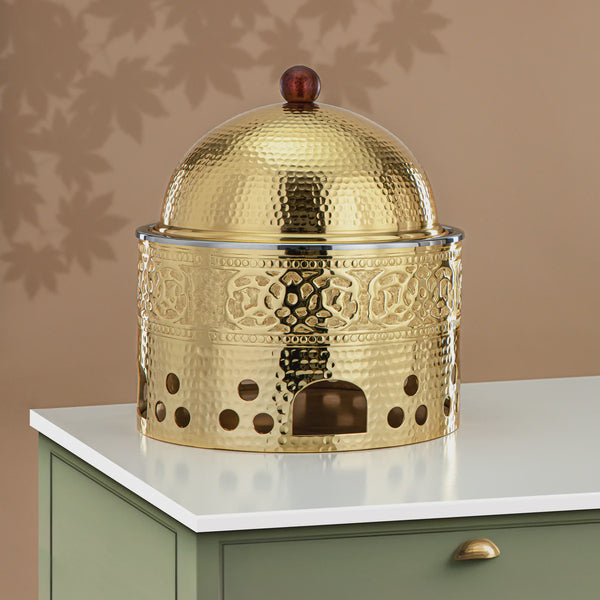 Decorative gold metal container with intricate patterns on a white surface against a beige wall.