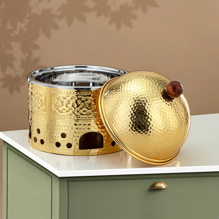 Gold and silver decorative container with a wooden knob on a beige surface.