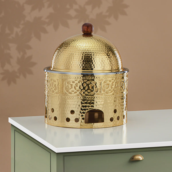 Decorative gold metal container with intricate patterns on a white surface against a beige wall.