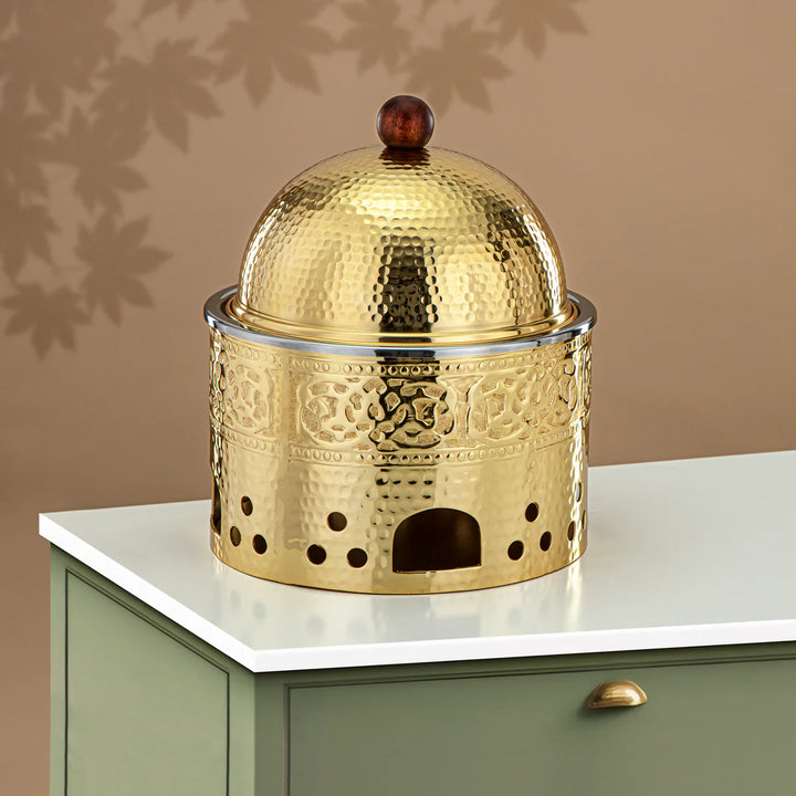 Gold metal incense burner with intricate designs on a white surface against a beige wall.