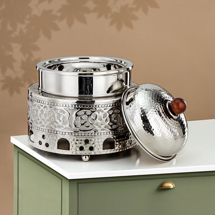 Decorative silver pot with intricate designs on a white surface against a beige wall.