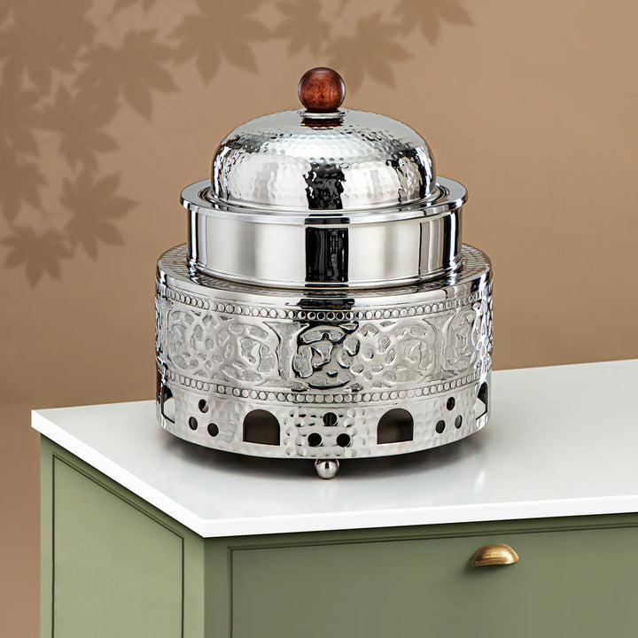 Decorative silver container with a domed lid on a white surface against a beige wall.