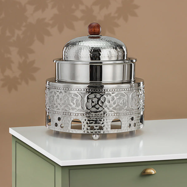 Decorative silver container with a glass lid on a white surface against a beige wall.