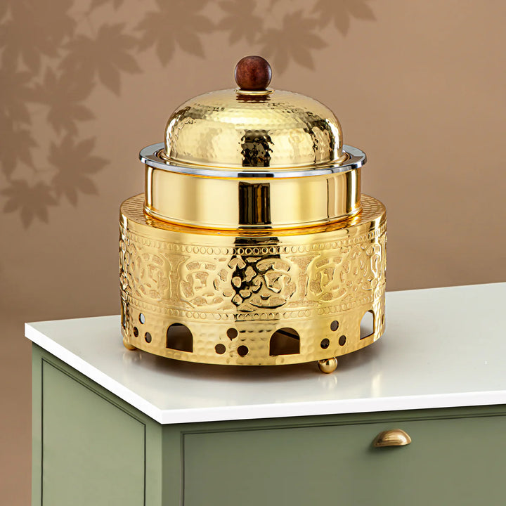 Gold decorative container with intricate patterns on a white surface against a beige wall.