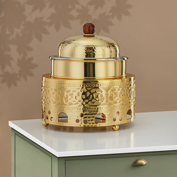 Gold decorative object with intricate patterns on a white surface against a beige wall.