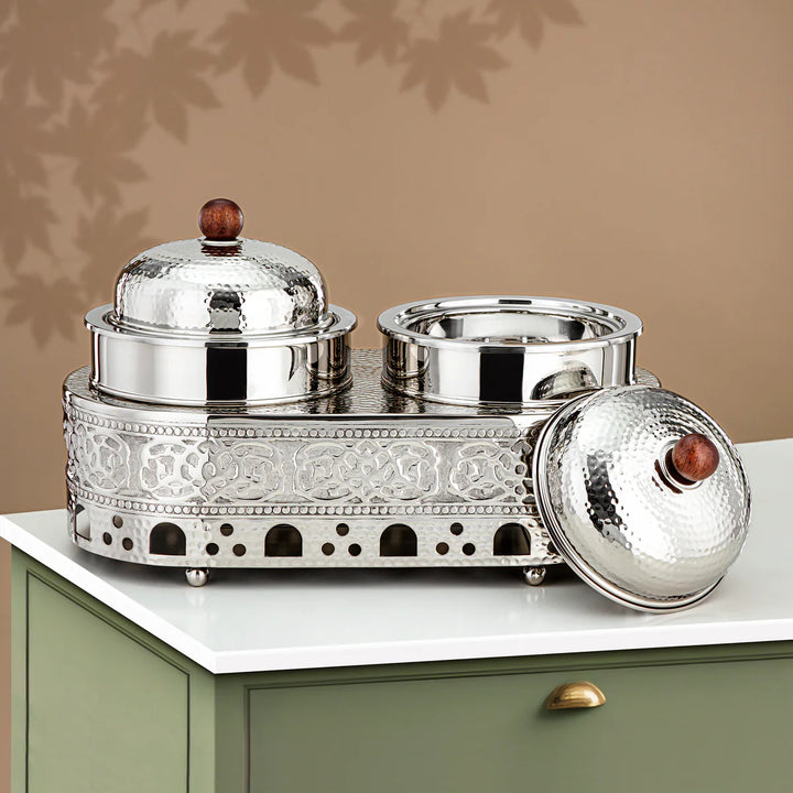 Decorative silver container with two lids on a white surface against a beige wall.