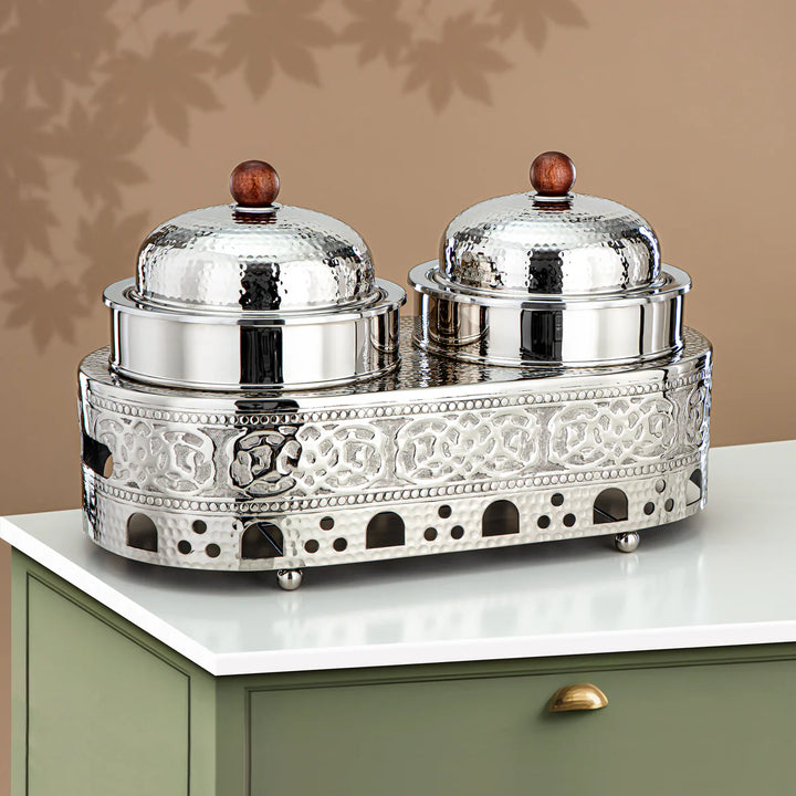 Decorative silver salt and pepper shaker set on a white surface with a beige wall background.
