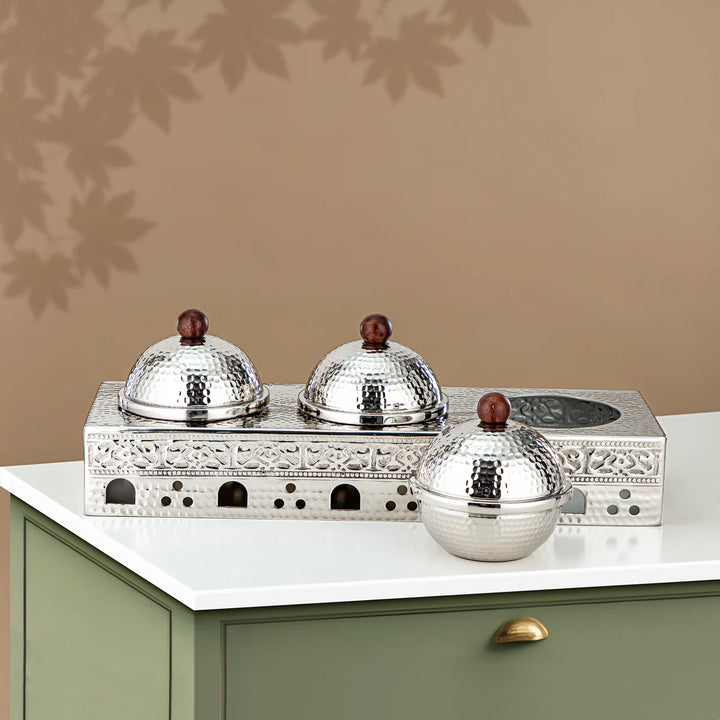 Decorative silver containers with wooden knobs on a white surface against a beige wall.