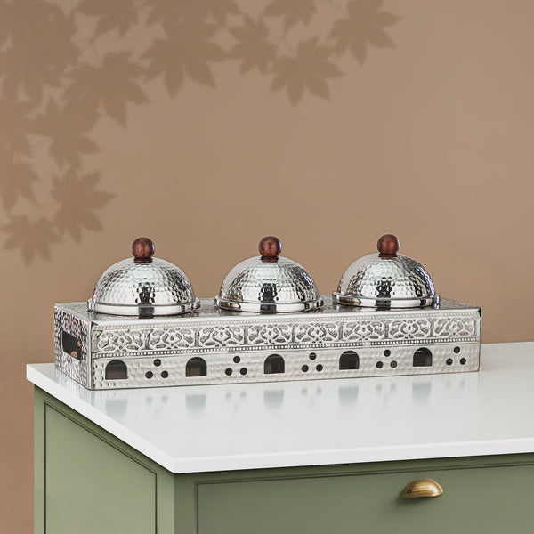 Decorative metal stand with three silver domes on a beige surface