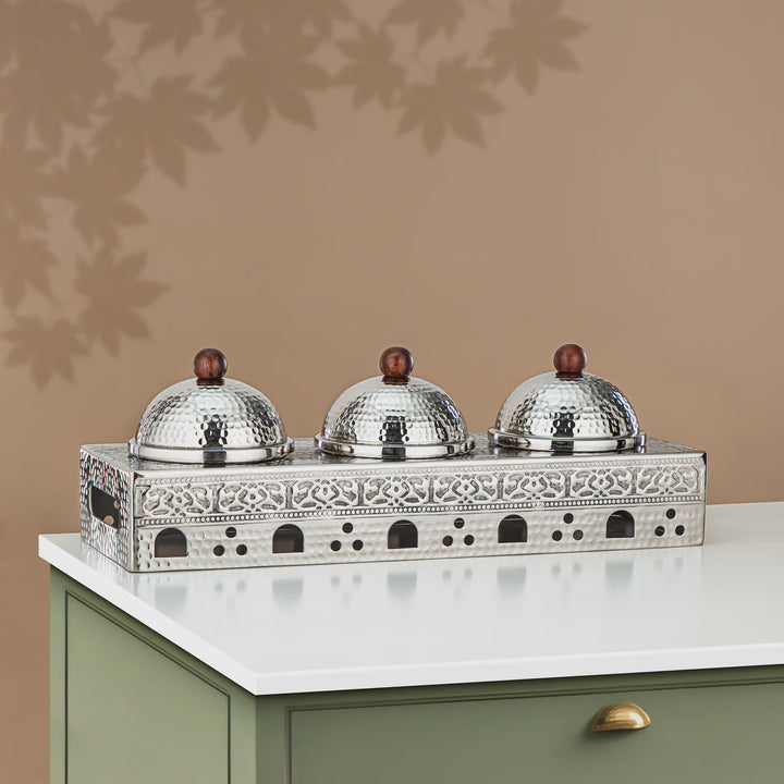 Decorative metal stand with three silver domes on a beige surface