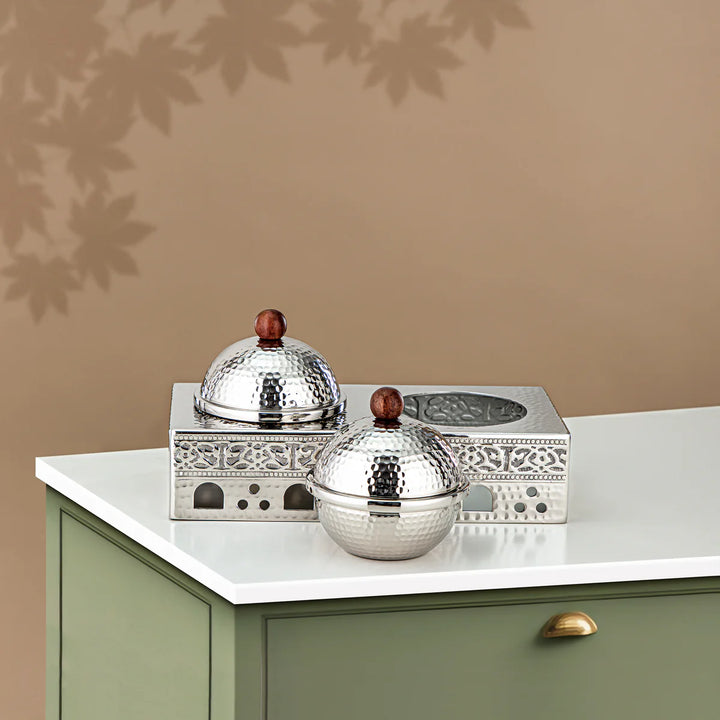 Decorative silver containers with wooden knobs on a white surface against a beige wall.