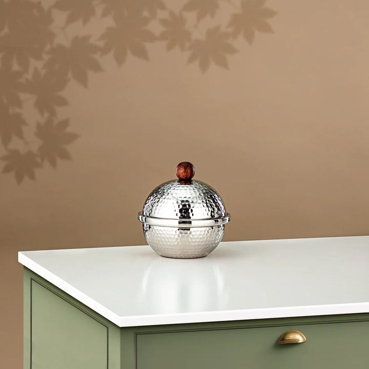 Silver decorative object on a white surface with a beige wall in the background