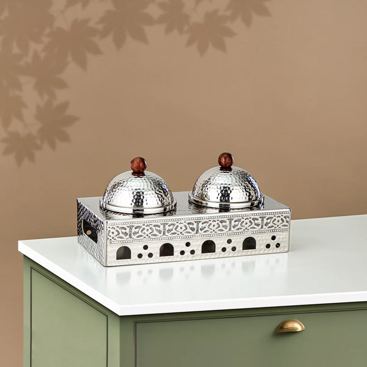 Decorative silver containers with wooden knobs on a patterned stand against a beige wall.