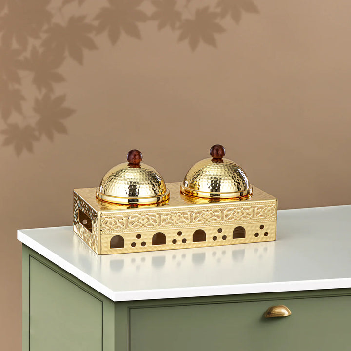 Decorative gold object with two domed covers on a white surface against a beige wall.