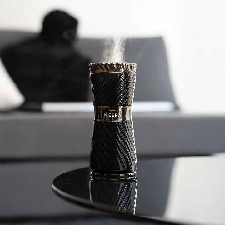 Black MEERA humidifier emitting steam on a reflective surface with a blurred background