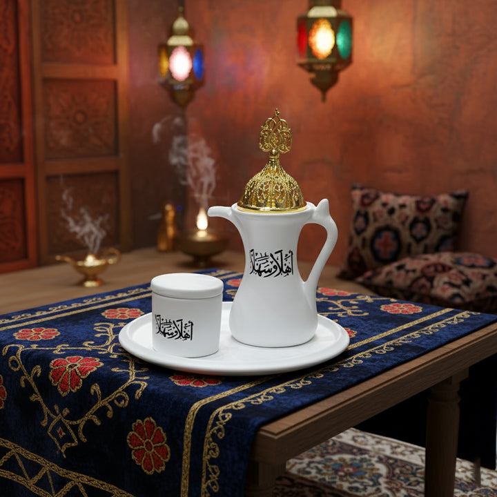 White coffee pot and cup with Arabic text on a tablecloth with decorative patterns.