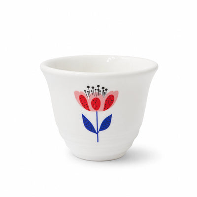 A white ceramic cup featuring a stylized floral design with red and pink petals, blue leaves, and black centers, set against a light gray background.